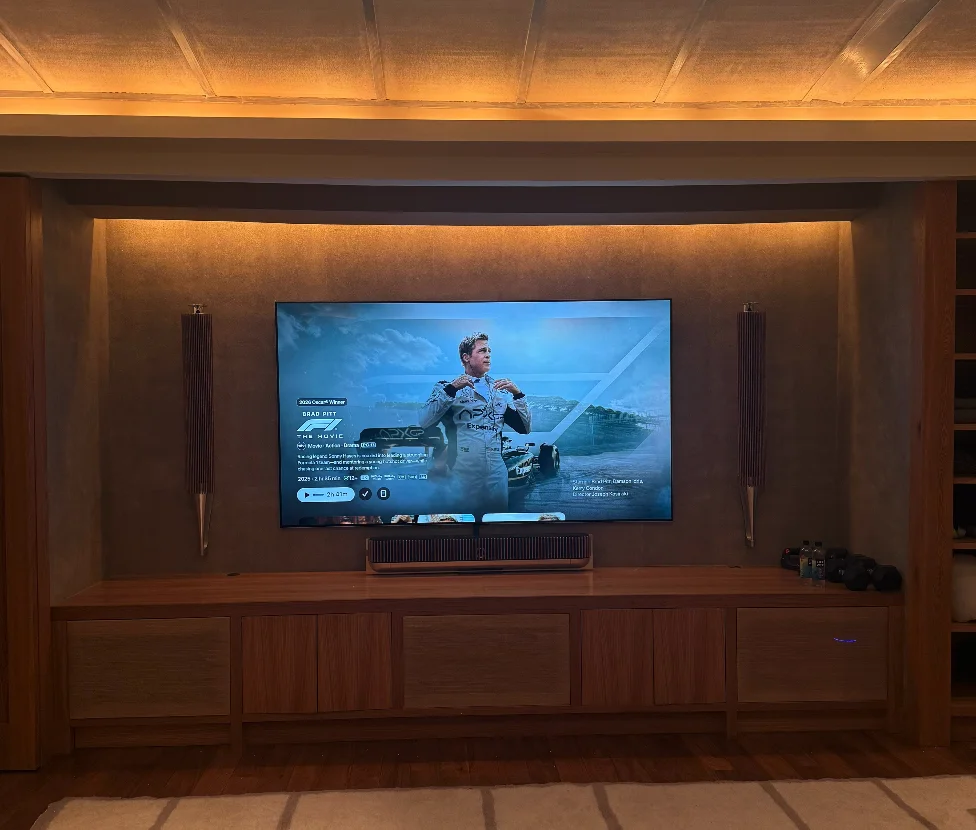 Luxury home theater with custom walnut built-in console, large flat-panel TV, and warm cove ceiling lighting