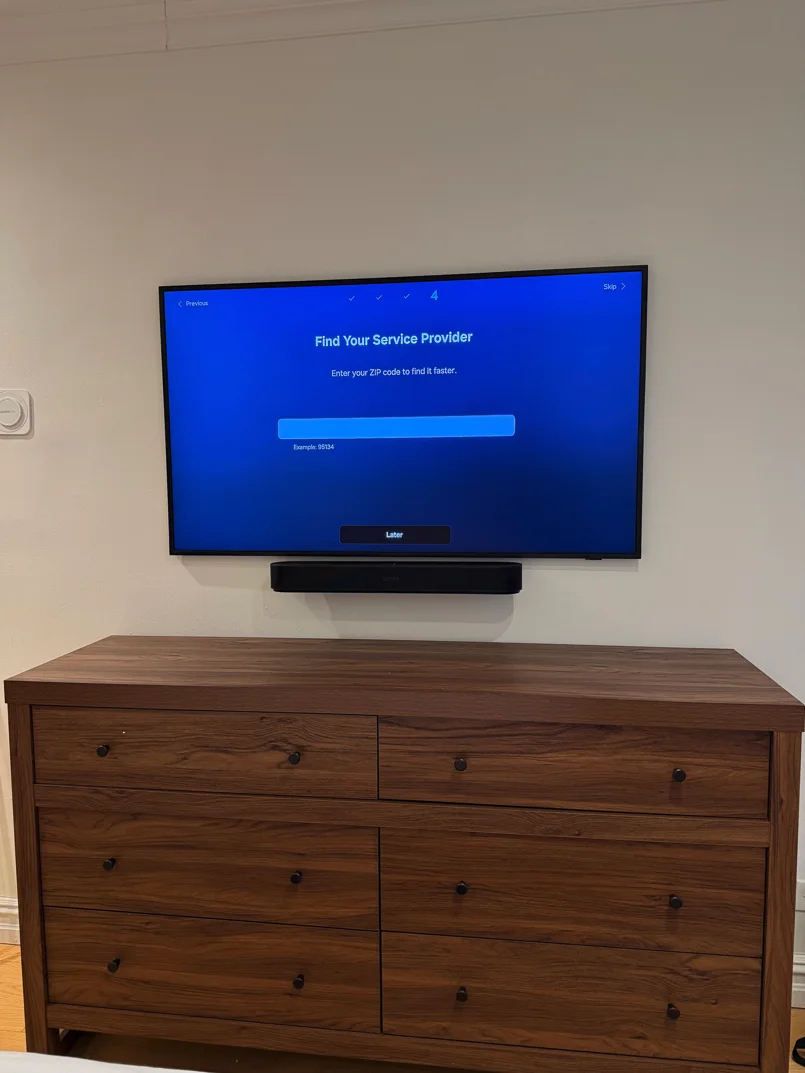 Wall-mounted flat-panel TV with soundbar above a walnut dresser in a residential bedroom